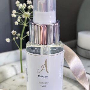 Clear perfume spray bottle on a marble surface with a pale pink ribbon; background includes small white flowers and soft lighting.