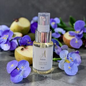 Perfume bottle with a silver ribbed collar and clear spray top, surrounded by purple flowers and pear halves in the background.