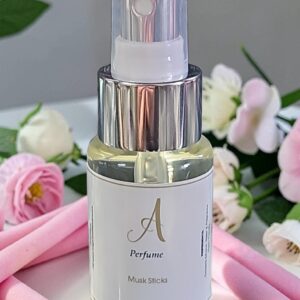 Clear perfume spray bottle with a silver cap and white label showing a stylized 'A' and 'Perfume' text, set against a backdrop of pink flowers and soft pink fabric.
