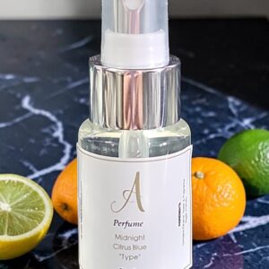 Clear perfume spray bottle on a marble surface with sliced oranges and limes nearby; bottle label reads Midnigth Citrus Blue 'Type' and 30 ml.