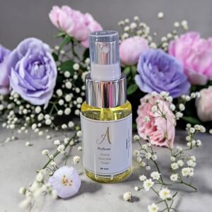 Clear glass perfume bottle with a spray nozzle, surrounded by pastel pink and lilac flowers and baby's breath.