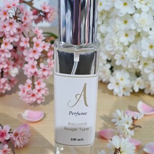 Clear glass perfume bottle with a shiny silver cap, labeled 'A Perfume' and 'Rouge Type', surrounded by pink and white blossoms.